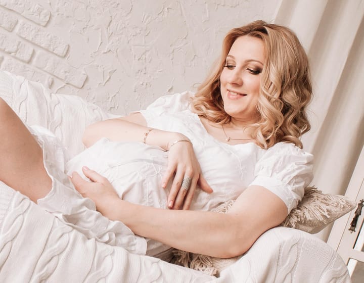 Mujer embarazada sonriendo en un sofá blanco